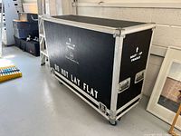 Wide angle view of the transport case showing the side panel with 'Do Not Lay Flat' warning and caster wheels.