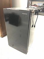 Front view of black Insignia mini fridge with power cord visible, showing overall condition including surface scratches.