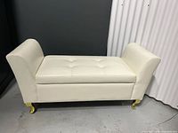 Front view of a cream vinyl covered bench showing button tufted seat and curved armrests.