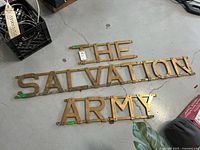Overview of three brass panels spelling THE, SALVATION, ARMY laid on floor