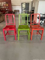 Front view of three chairs (red, green, orange) aligned side by side on concrete floor