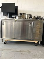 Front view of stainless steel station showing sliding doors, drawers, and caster base