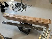 Box of linear lights with one linear light fixture removed and resting on top of the box, showing the packaging labeled 'LINEAR LIGHT' and the brand Monte Carlo.