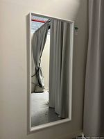 Full view of the rectangular wall mirror mounted on a wall with white frame and reflective glass surface.