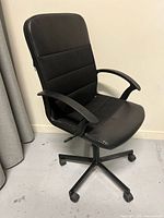 Front angle view of black upholstered Ikea office chair with padded seat, backrest, armrests, and caster wheels.