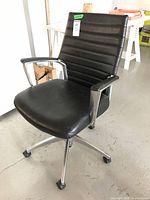 Front diagonal view of black vinyl office chair showing metal frame, armrests with padding, and caster wheels.