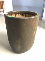 Large brown glazed pottery planter with drip glaze detail on inner rim, standing on light floor in large room.