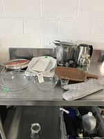 Photo of assorted kitchen items on metal surface showing glass bowls, serving trays, ice bucket, kettle, fan, and accessories