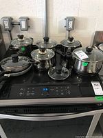 Overview of cookware on induction stove showing two stacked T-Fal frying pans alongside stainless pots, steamer insert and lids