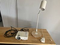 Wide view of wooden table with white Jinghoo projector and IKEA desk lamp on top, showing projector cables and lamp shapes.