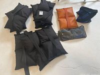 Overview of 10 sandbags in mostly black fabric, one brown, and one dark blue, laid on floor showing various shapes and handles