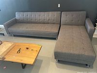 Front and angled view of the sectional couch showing both pieces elevated on shiny chrome metal legs, gray tufted fabric upholstery, and some visible stains.