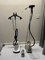Overview of two garment steamers and steam iron on floor against wall