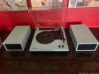 Full view of the LP&No.1 turntable and two matching speakers on a dark surface with red wall background.