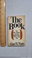 Front cover of the 1966 Alan Watts paperback book titled 'The Book'. Shows author and title prominently, with a ruler for size reference.