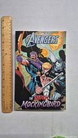 Front cover of Avengers The Death of Mockingbird paperback comic book with a wooden ruler for scale.