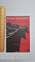 Front cover of Batman Year One paperback showing title, author names Frank Miller and David Mazzucchelli, with Batman artwork in black and red.