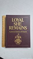 Front cover of the book showing title 'Loyal She Remains: A Pictorial History of Ontario' with a decorative crest at the bottom. Book placed beside a ruler showing height.