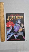 Front cover of the graphic novel Just Beyond by R.L. Stine showing children and a dark figure, with a ruler for size reference.