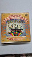 Front cover image of The Beatles Magical Mystery Tour vinyl record with colorful psychedelic design and text.