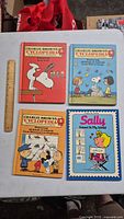 Front covers of four vintage Charlie Brown books laid flat with a ruler beside them to show scale.