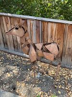 Full side view of the life-size metal deer sculpture assembled from rusted steel plates standing against a wooden fence