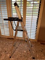 Side view of 3-step aluminum ladder showing steps, black plastic tool tray on top, and rubber feet caps