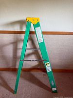 Front view of the green and yellow 3 step ladder showing the side frame and safety instructions.