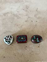 Three small vintage porcelain trinket boxes arranged in a row on a light surface, showing front and top floral designs.