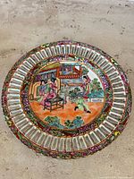 Top view of the antique Famille Rose medallion plate showing central painted scene with figures and garden gazebo, reticulated edge, and floral border.