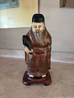 Front view of the hand carved and hand painted wooden Chinese figurine on wooden stand showing detailed facial features and attire.