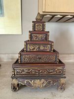 Front view of tiered wooden herbal chest showing carved gilt decorative panels and finial on top.