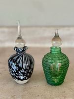 Front view of two Murano glass perfume bottles, one black and white with tall stopper, one green with rounded stopper.