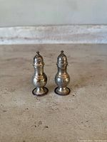 Pair of antique sterling silver salt and pepper shakers viewed from front on a stone surface.