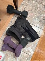 Photo of two pairs of dumbbells in black and purple neoprene coating, and a pair of black adjustable fabric ankle or wrist weights on a tiled floor.