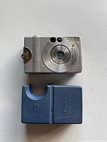 Top view of Canon PowerShot S110 Digital Elph camera in silver along with Canon battery charger in dark blue color.