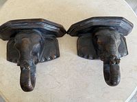 Top view of two carved wooden elephant head wall shelves showing detailed carving and shelf surface.