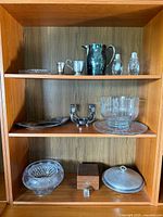 Full view of wooden shelf containing silver and crystal items arranged on three shelves.