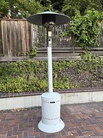 Full view of the standing white metal patio heater with cylindrical base and wide heat reflector on top.