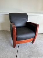 Side angle showing black leather seat and backrest, curved wooden armrests and front support.