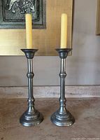 Front view of two tall silver tone vintage candlestick holders with yellow candles on a living room surface.