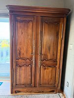Front view showing two paneled wooden doors with metal handles and carved decorative elements on top and base.