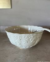 Side view of the white ceramic punch bowl showing embossed floral and ribbon decorations on the exterior
