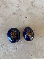 Two Limoges porcelain trinket boxes on beige surface, one oval and one round, cobalt blue with gold floral pattern.