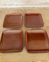 Four reddish-brown square sushi plates arranged on a countertop, showing their glossy surface and color gradation.