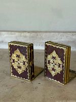 Pair of Italian gold gilt folding bookends with brown and gold ornate detailing, angled to show front and side folds.