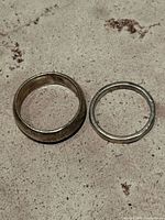 Two sterling silver rings placed on a textured surface; one wide band and one thin band with visible tarnish and wear.