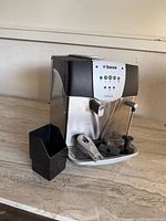 Frontal view of the Saeco Italia espresso machine with black plastic container and tamper tool