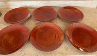 Photo of six large stoneware plates arranged in two rows of three, showing red glaze variation and mid century style design.