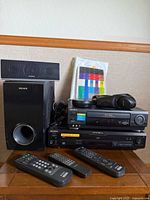 Sony home entertainment lot with VCR, DVD/CD Video CD player, subwoofer, center speaker, remote controls, and headphones arranged on wooden surface.